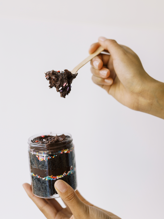 Hand holding a small jar of soil with a wooden stick, against a plain background