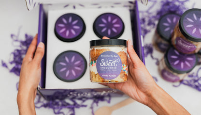 Person holding a jar of a Sweet Encounter gluten free cake with a box of similar jars in the background